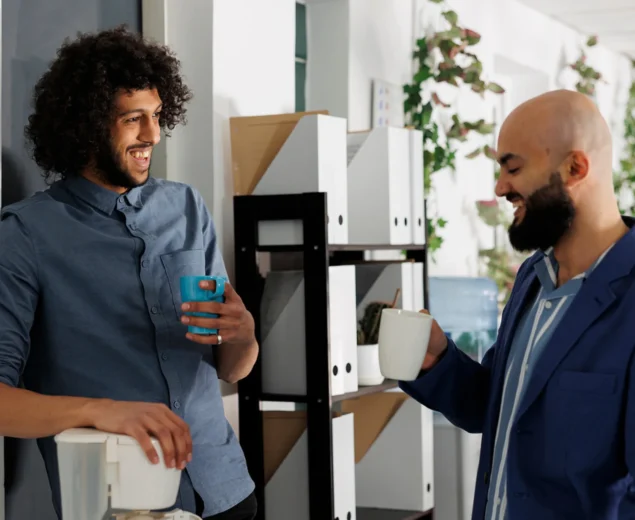 two men drink coffee in office