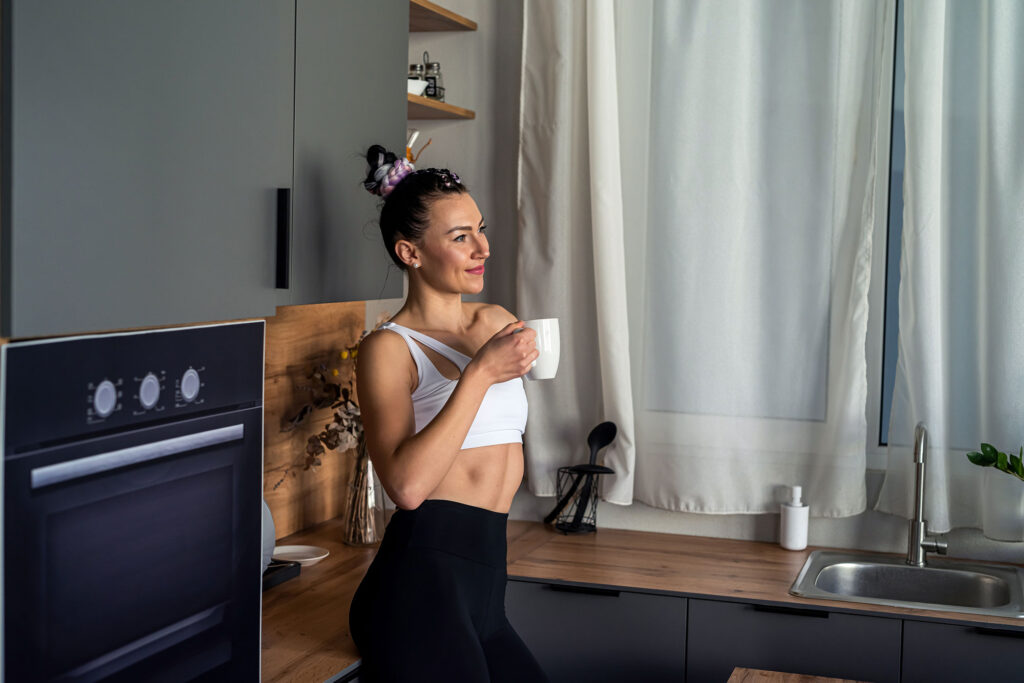 woman in workout clothes drinking coffee in kitchen