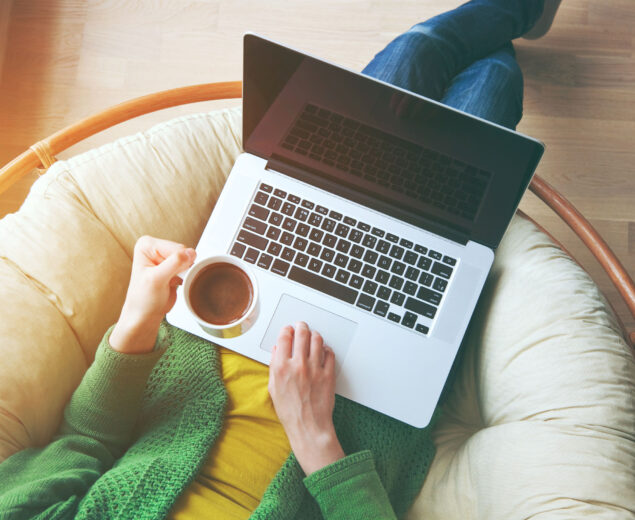 woman sitting i papasan chair with coffee and laptop