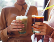 two women clicking iced coffee glasses