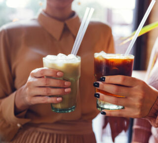 two women clicking iced coffee glasses